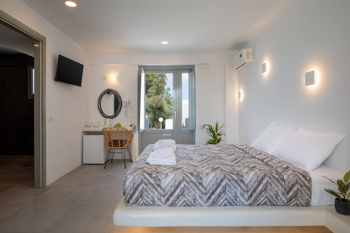 Quarto com cama, escrivaninha, cadeira, televisão e janela.