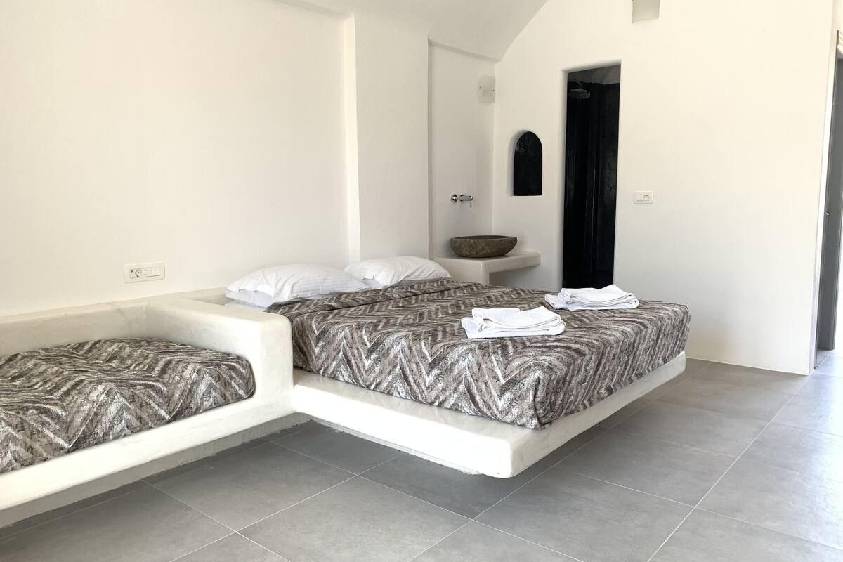 Quarto moderno com duas camas, uma pia pequena e uma porta escura.