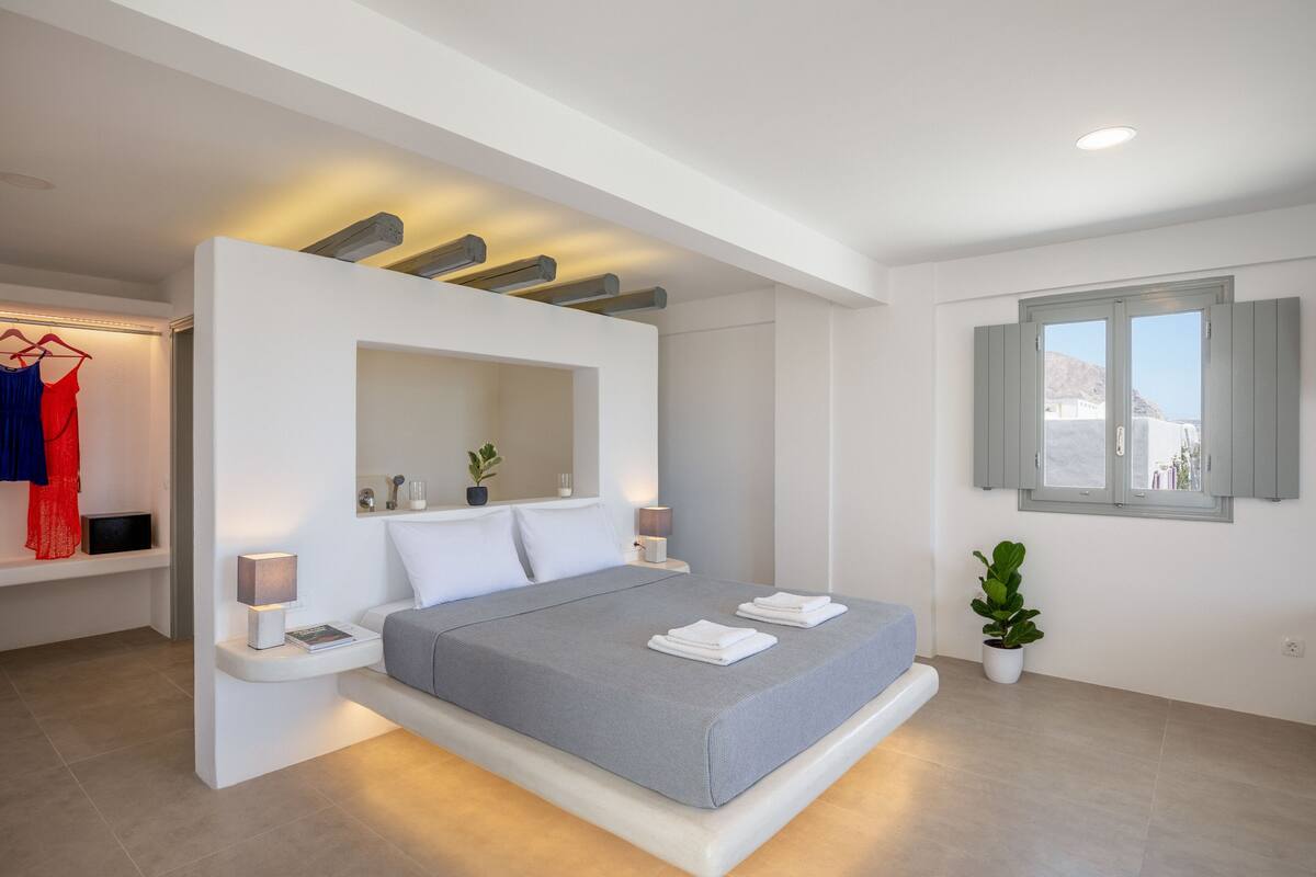 Quarto moderno com uma cama grande, mesas de cabeceira, um espelho e uma janela com persianas.