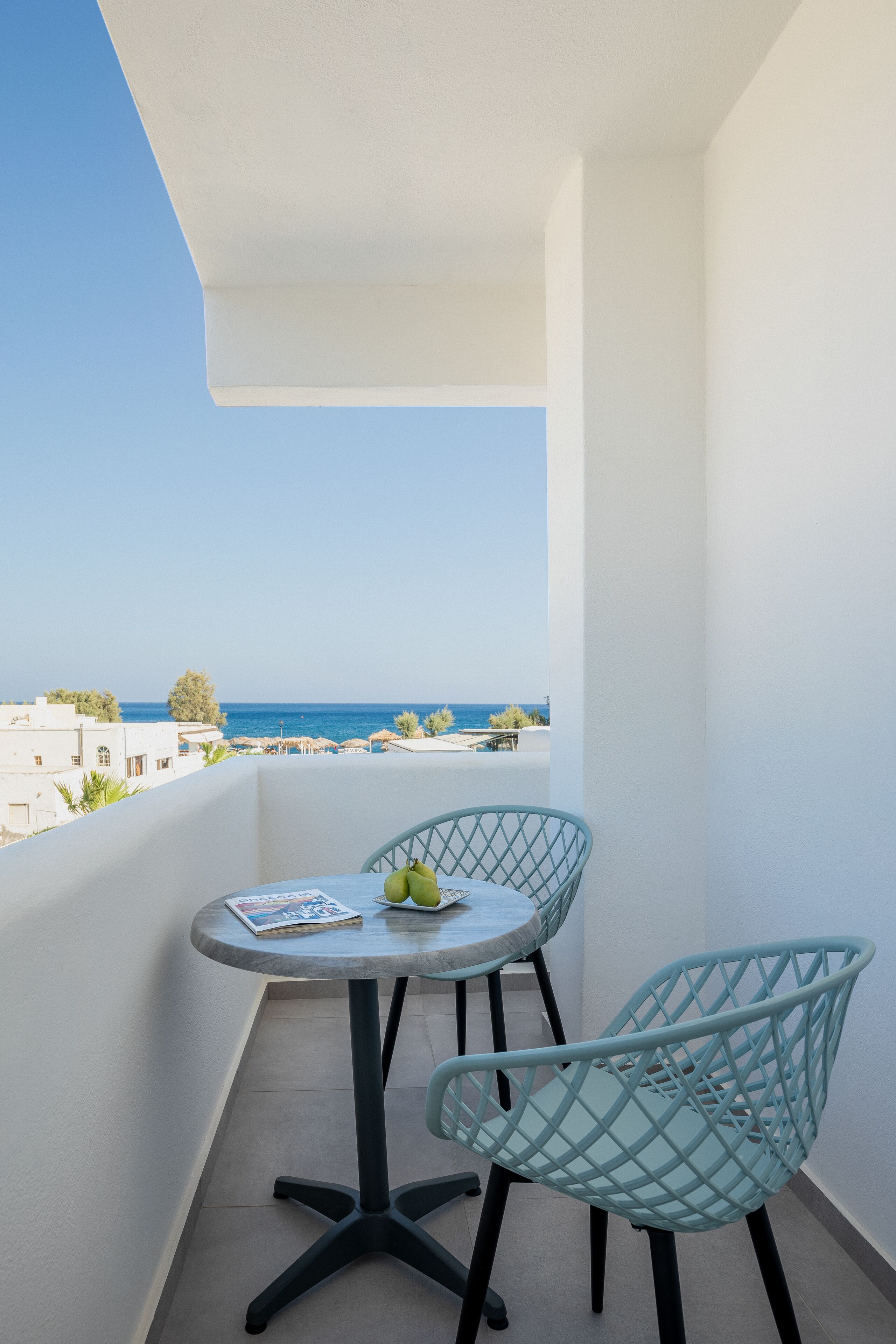 A balcony with a round table and two chairs, overlooking a coastal view.