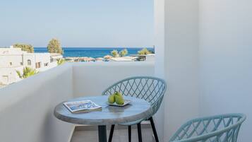 A balcony with a round table and two chairs, overlooking a coastal view.