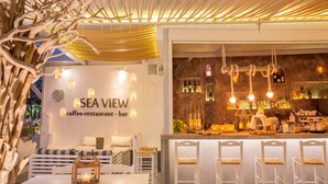 A cozy cafe with a bar area, seating, and a view of the sea. -  Sea View Bay Hotel Santorini (Santorini)