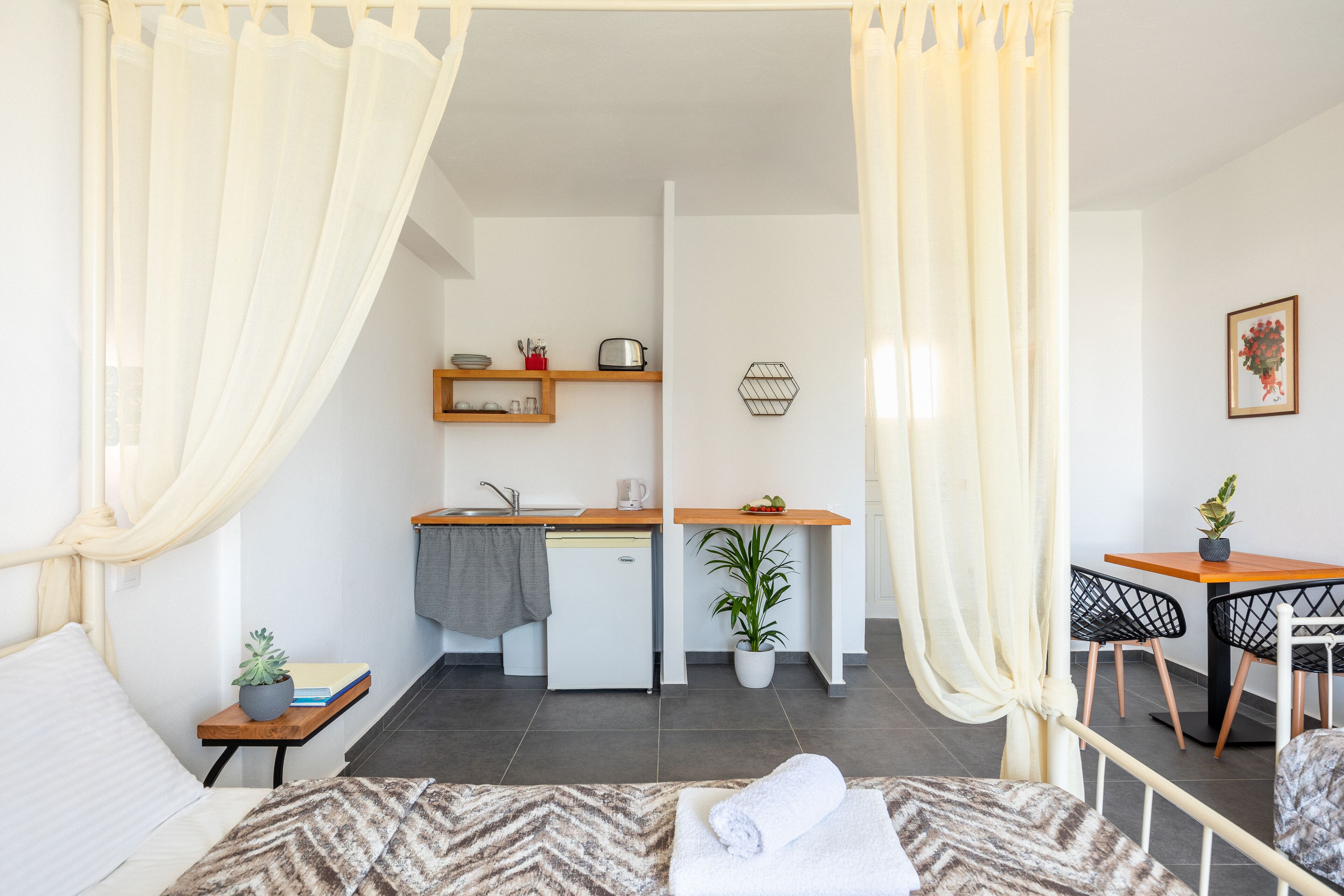 Un dormitorio con cama, una mesita de noche con una planta y vistas a una kitchenette.