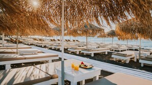 A beachside lounge area with white lounge chairs and tables, some with drinks and fruit. -  Sea View Bay Hotel Santorini (Santorini)
