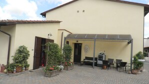 Un edificio con un patio techado, mobiliario exterior y plantas en macetas.