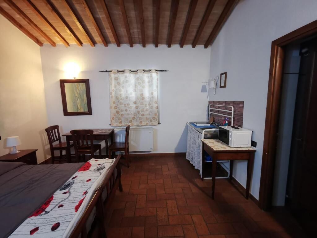 A small, cozy room with a bed, a wooden table, a chair, a desk with a computer, and a radiator.