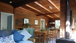 A cozy cabin interior with a wooden ceiling, a dining area, a sofa with cushions, and a wood-burning stove. - Allenvale (Lorne)