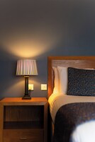 A neatly made bed with a patterned pillow, a bedside lamp, and a wooden nightstand with a drawer.