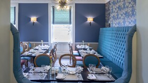 Un comedor con una mesa larga dispuesta para una comida, asientos tapizados en azul e iluminación montada en la pared.