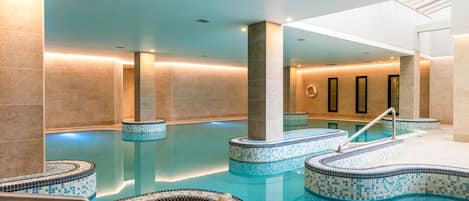 Una amplia piscina interior con múltiples accesos y suelo de baldosas.