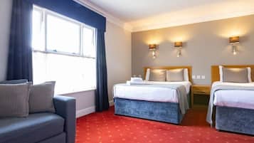 A hotel room with two beds, a sofa, and a window with curtains.