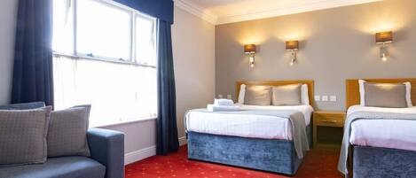 Quarto de hotel com duas camas, um sofá e uma janela com cortinas.