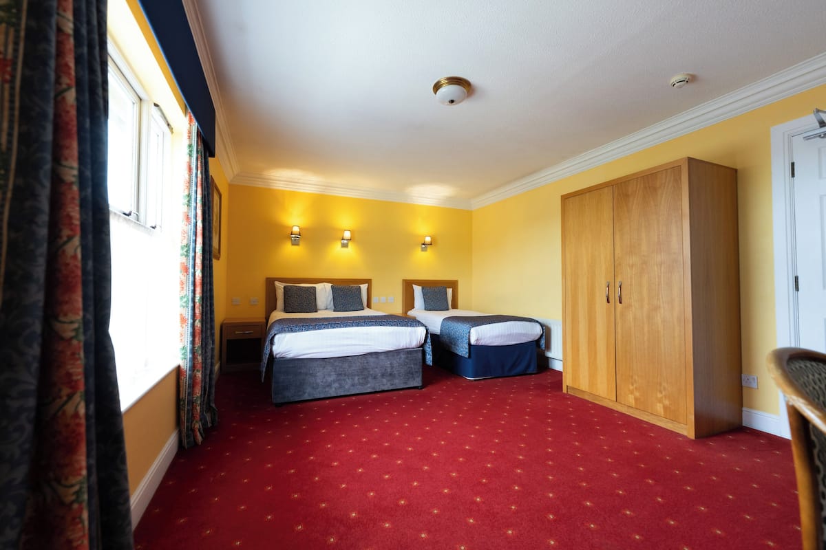 Une chambre d’hôtel avec deux lits, une armoire et une moquette rouge.