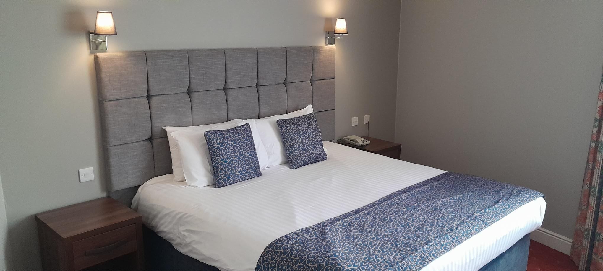 A neatly made bed with a grey upholstered headboard, two bedside tables, and a patterned bedspread.