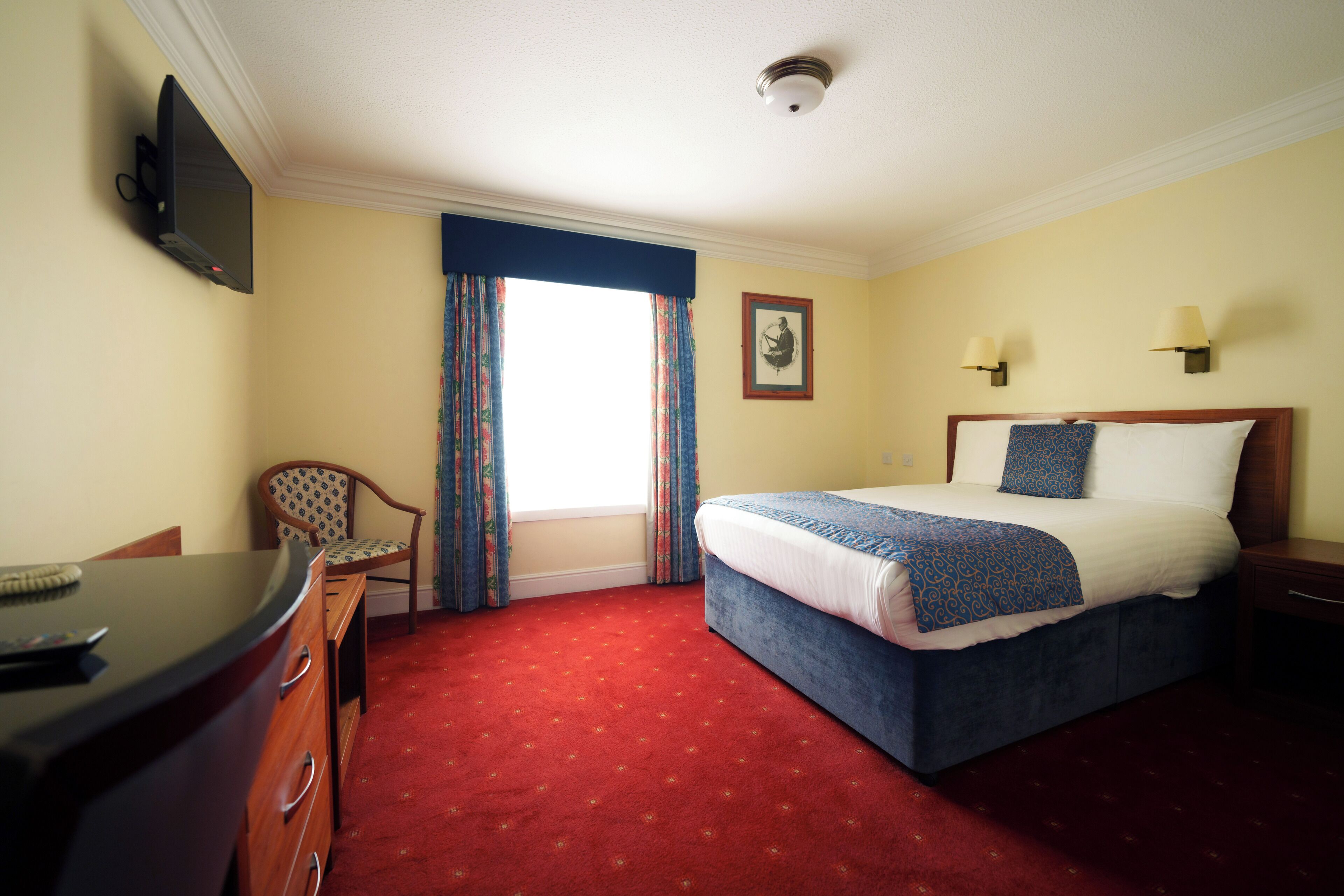 A hotel room with a bed, a desk, a chair, a television, and a window with curtains.