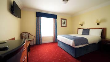 A hotel room with a bed, a desk, a chair, a television, and a window with curtains.