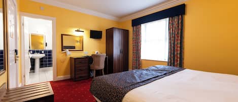 A hotel room with a bed, a desk, a chair, a wardrobe, a mirror, and a bathroom visible through an open door.