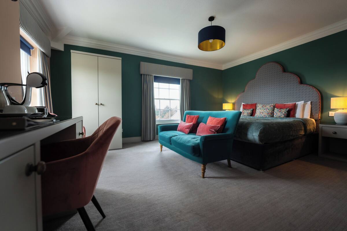 Une chambre avec un canapé de couleur turquoise, un lit agrémenté d’oreillers à motifs, un bureau avec une lampe et une armoire.