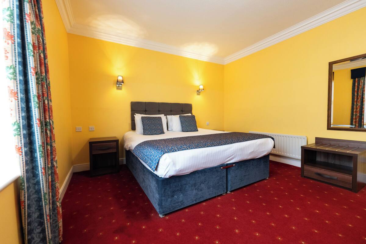 Une chambre avec un grand lit, des murs jaunes et une moquette rouge.