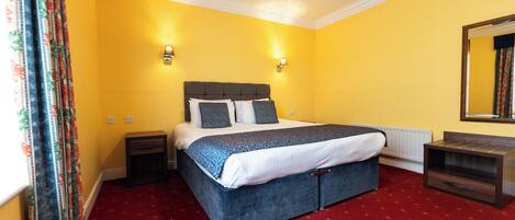 A bedroom with a large bed, yellow walls, and red carpet.