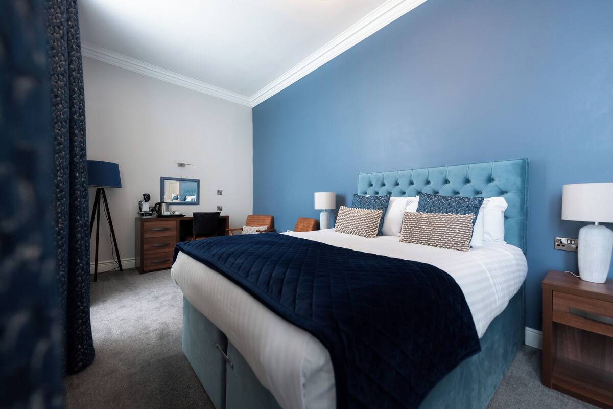 Une chambre à coucher avec un grand lit, un bureau, une chaise et une lampe.