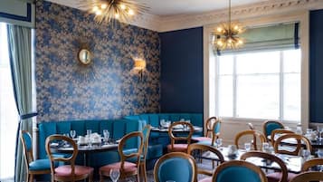 A restaurant with blue upholstered booths and wooden chairs, a patterned wall, and chandeliers.