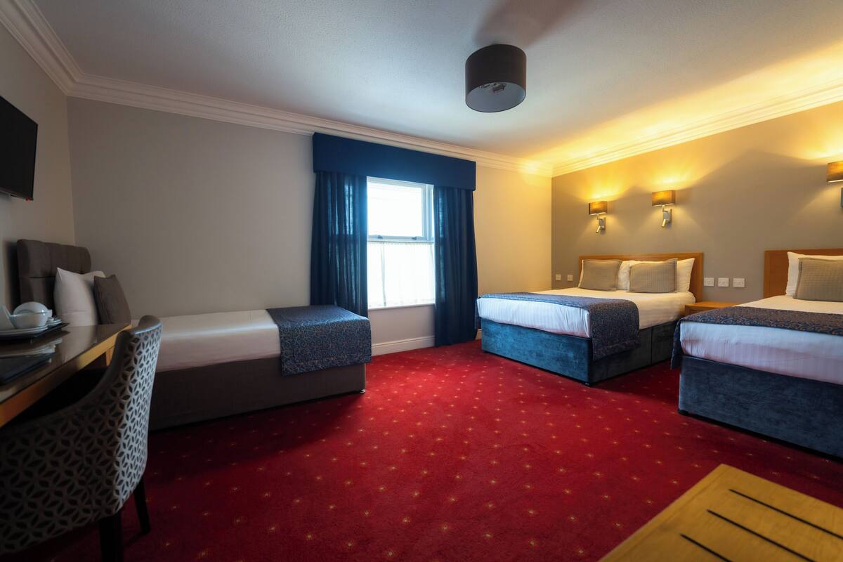 Une chambre d’hôtel avec deux lits, un bureau, une chaise et une fenêtre avec des rideaux.