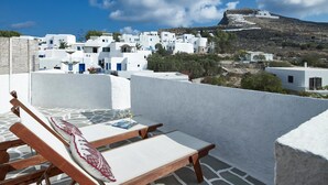 Une terrasse avec un fauteuil et une table, donnant sur un village aux maisons blanchies à la chaux, avec une colline en arrière-plan.
