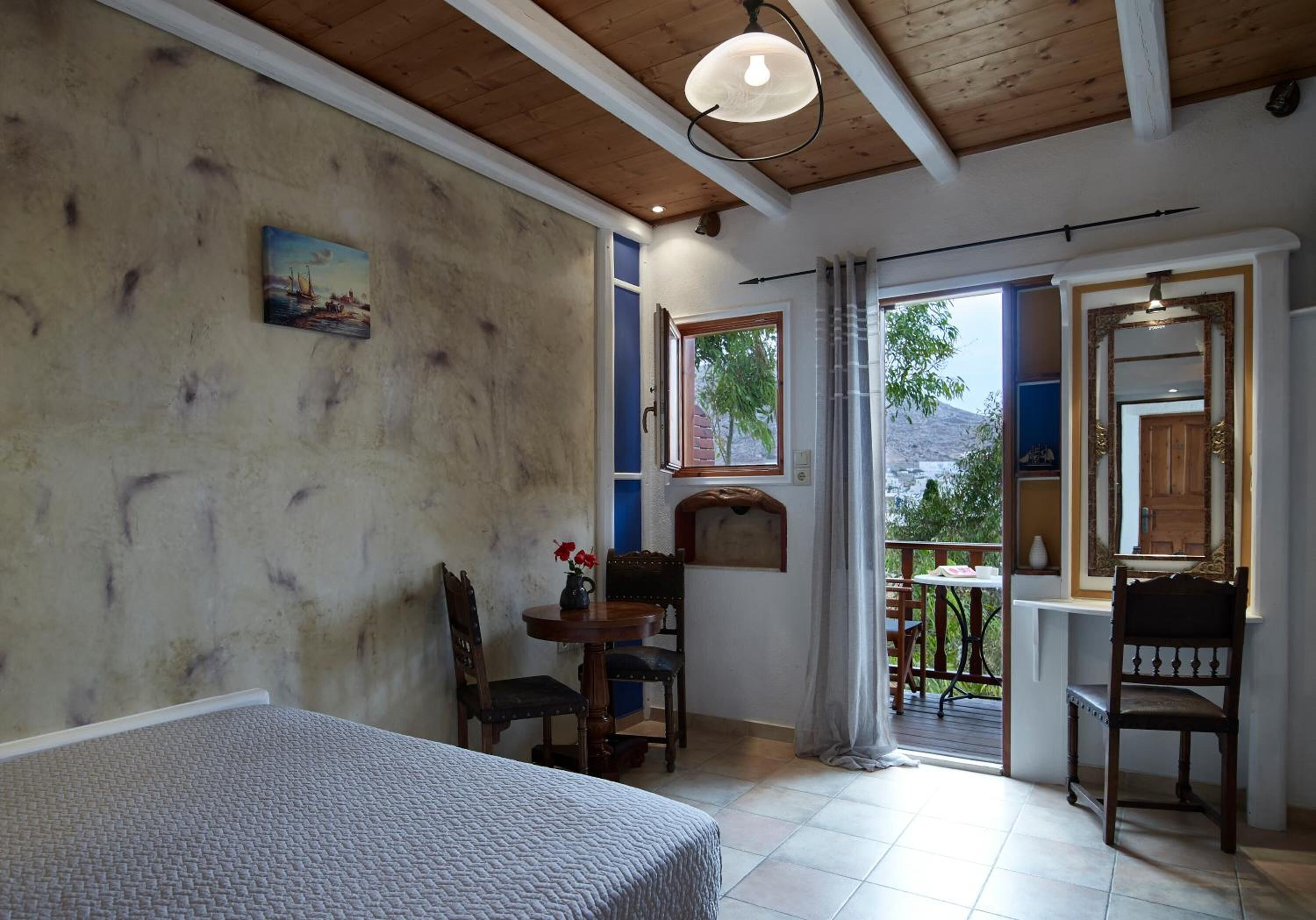 A bedroom with a bed, a desk, and a chair. There is a window with a view of the outdoors.