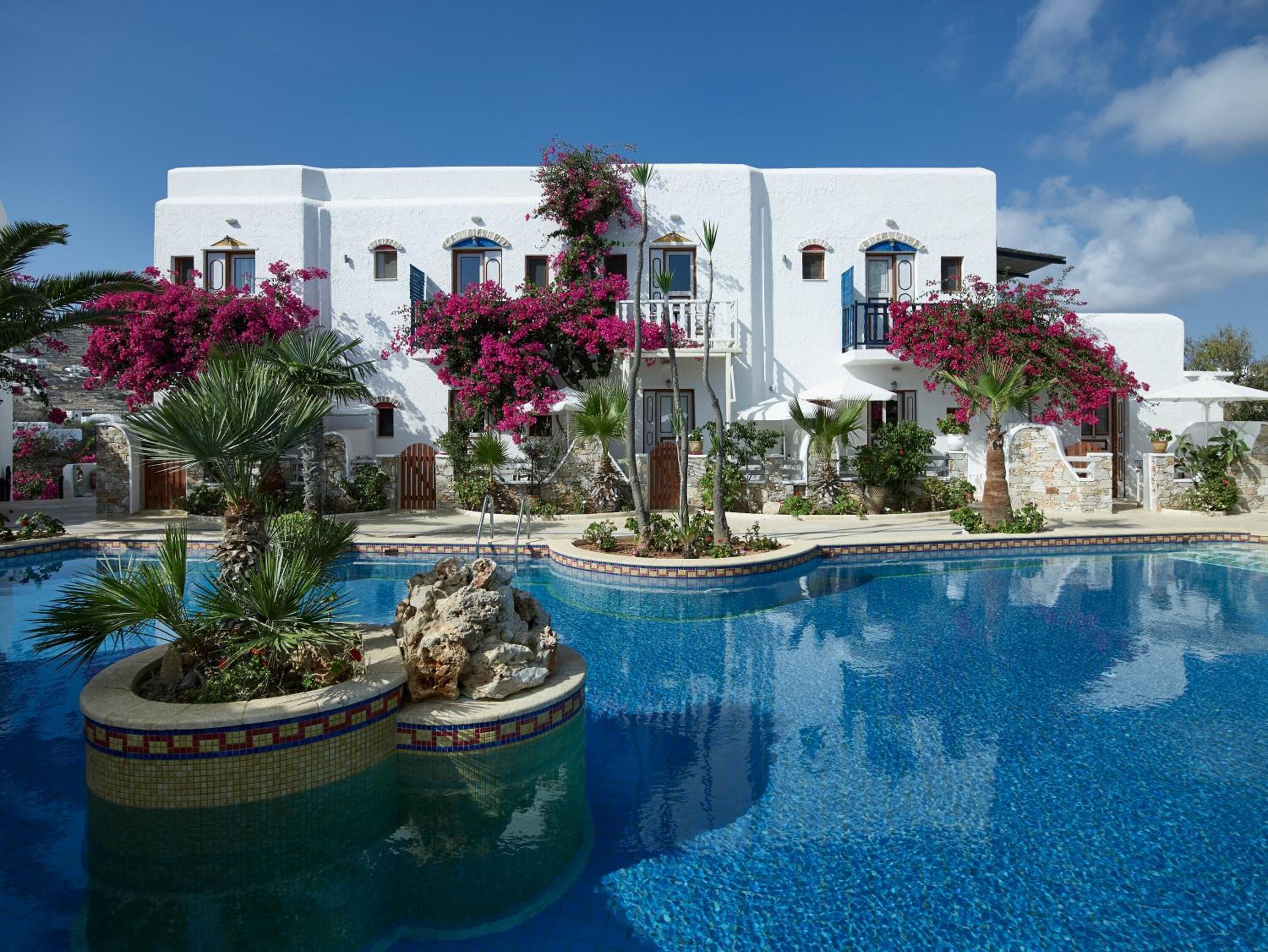 Un edificio blanco con balcones, piscina y flores de buganvilla rosadas.