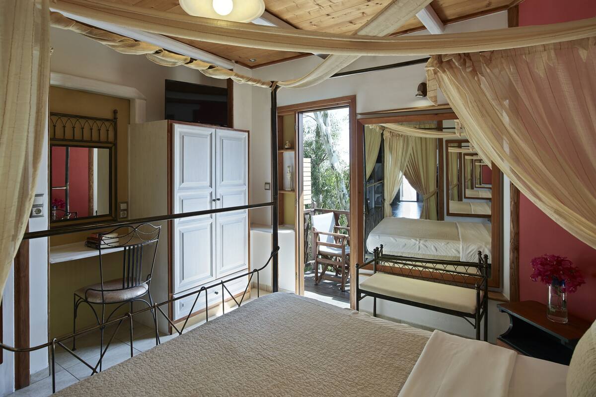 Une chambre à coucher avec un lit, un bureau et une chaise. On y trouve également une armoire, un miroir et une fenêtre avec des rideaux.