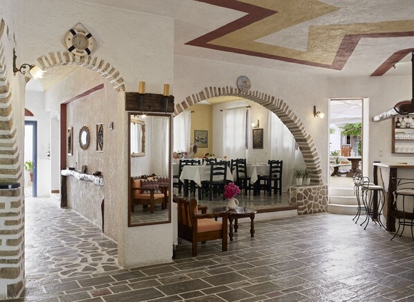 A spacious dining area with high ceilings, stone walls, and a mix of wooden and metal furniture. - Hotel Polikandia (Folegandros)
