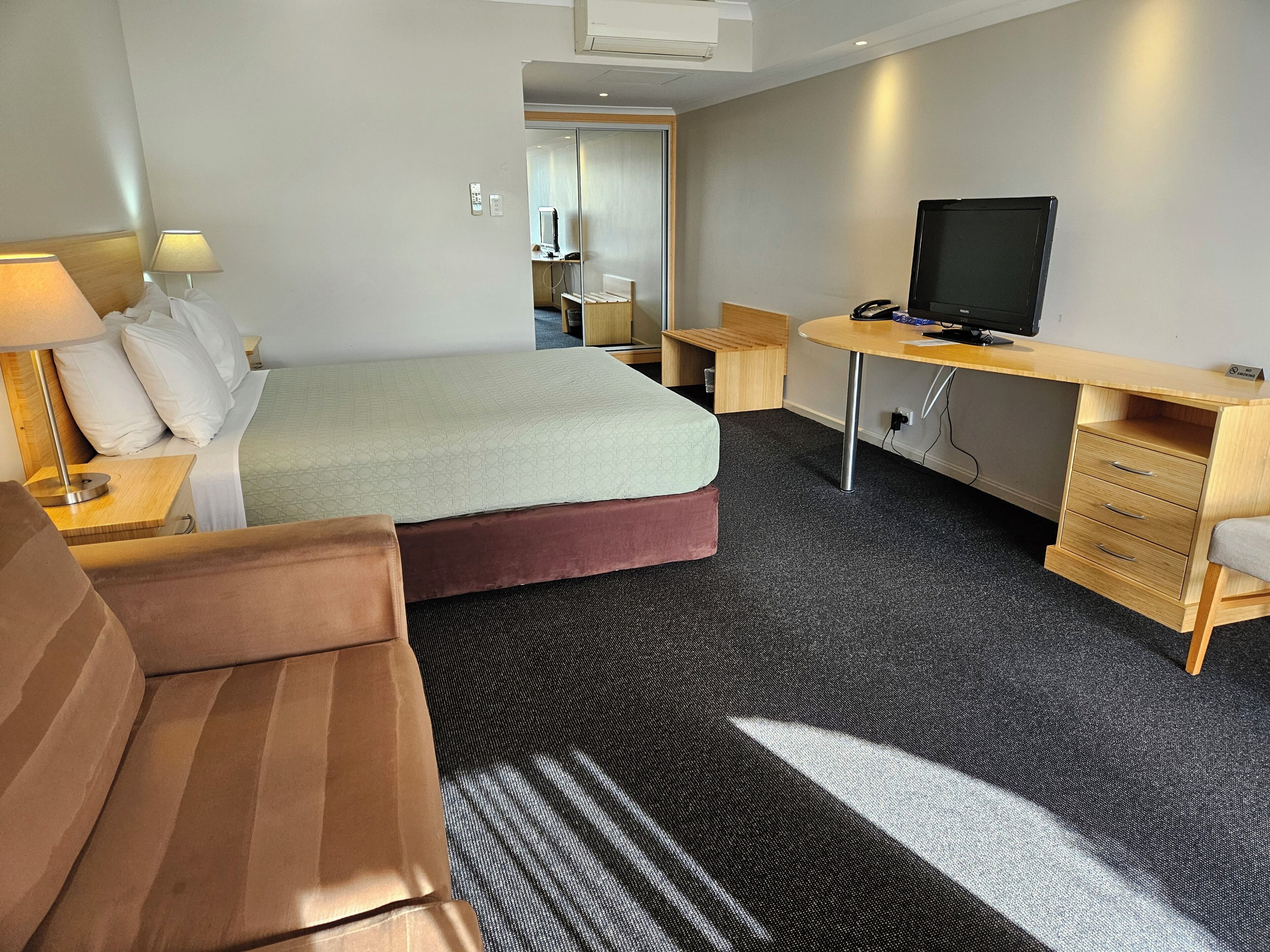 Une chambre d’hôtel avec un lit, un bureau, une télévision, un canapé et un sol recouvert de moquette.
