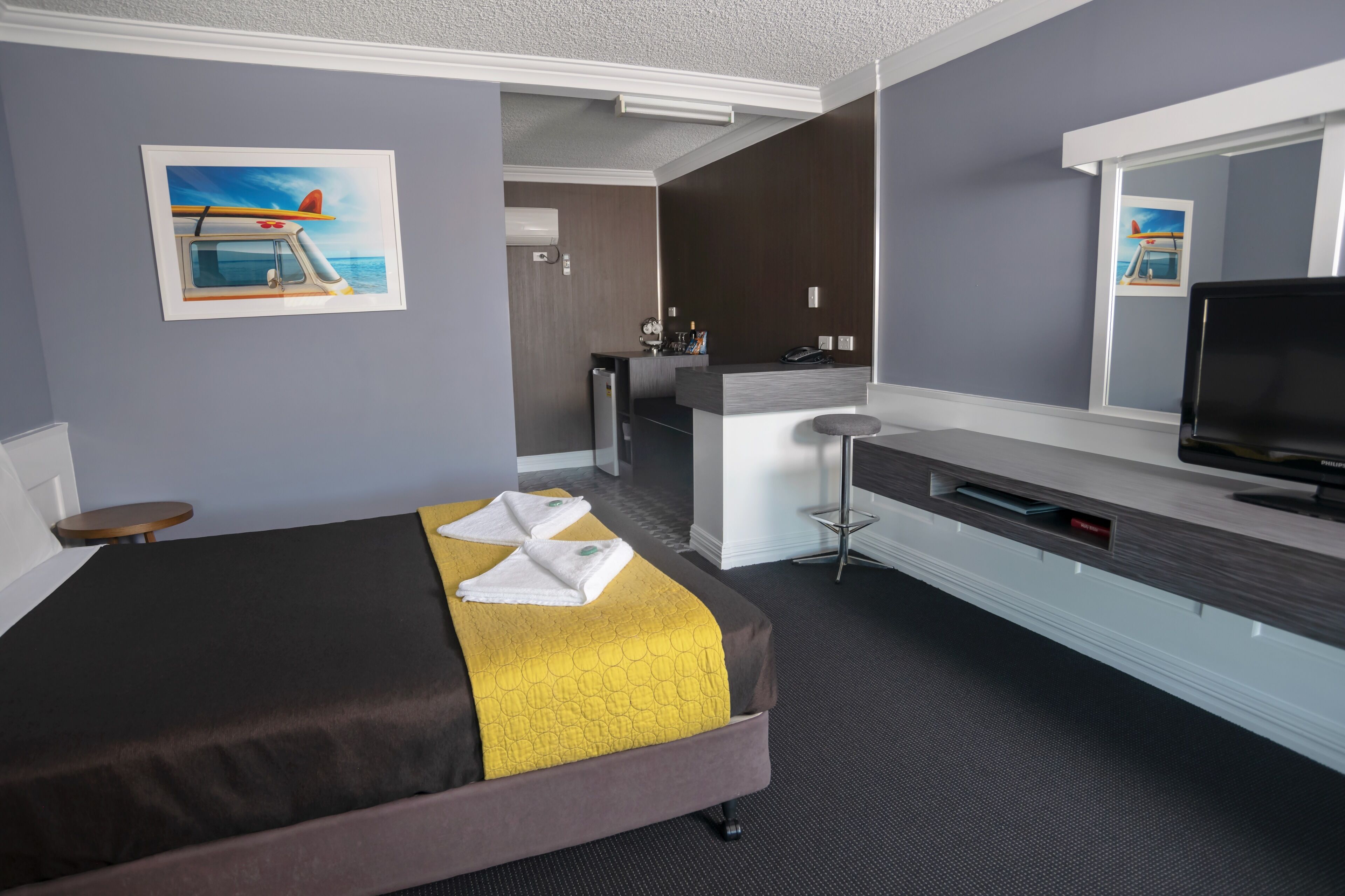 Habitación de hotel con una cama, un escritorio, un televisor y un cuadro de un barco en la pared.