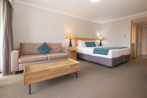 Ein Hotelzimmer mit einer Couch, einem Bett, einem Holztisch und zwei Nachttischlampen.