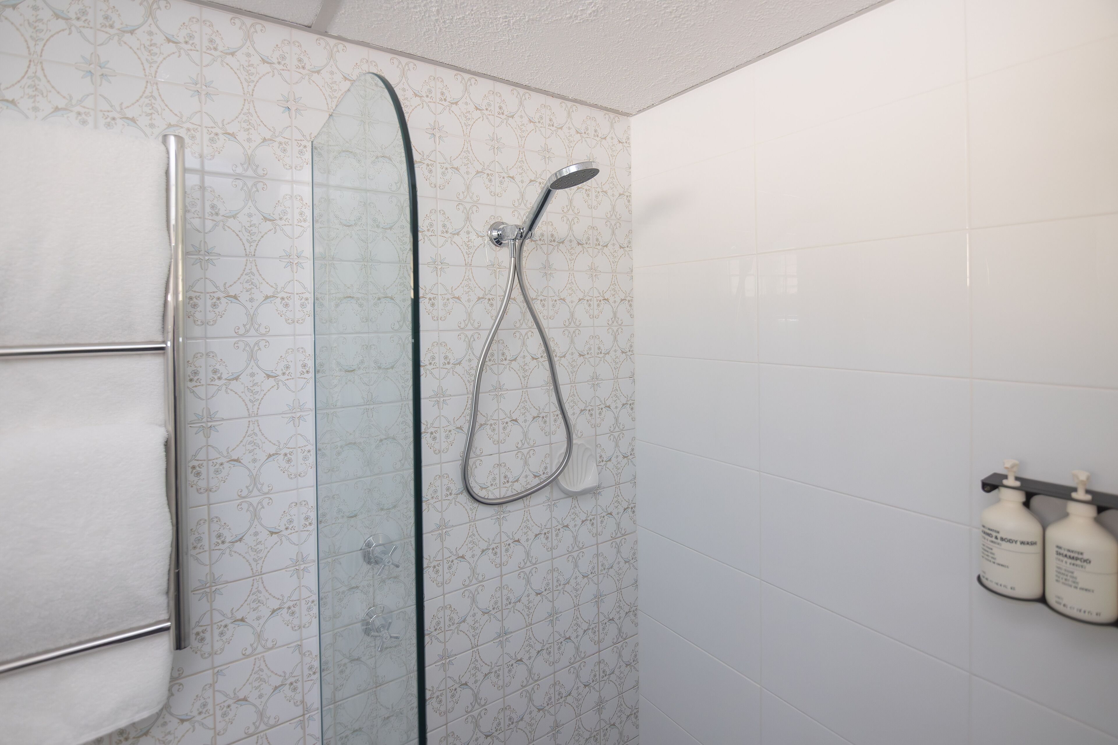 A shower with a glass door, a towel rack, and two bottles of shampoo on the wall.