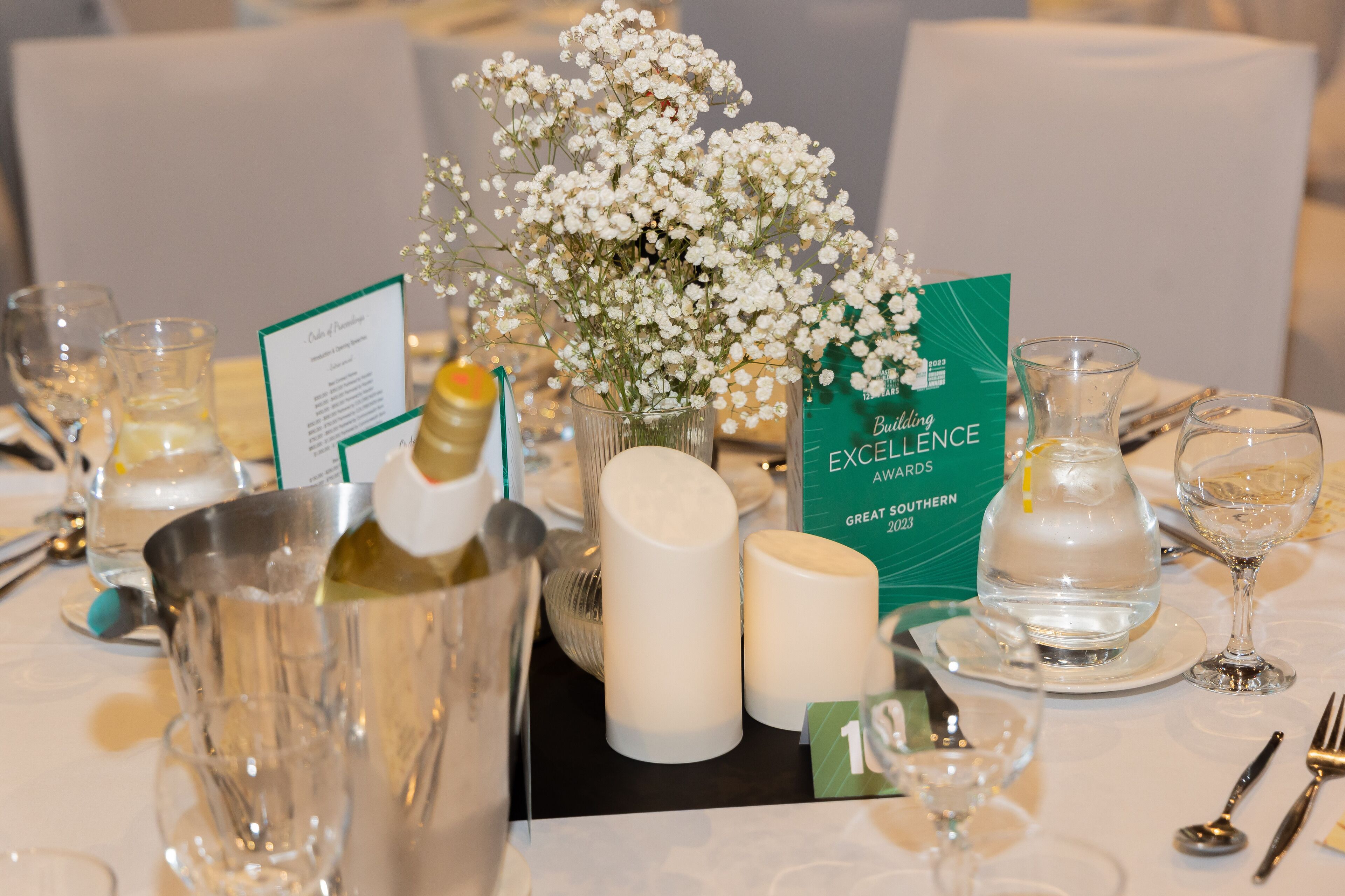 A table set for a formal event with a menu, a vase of flowers, candles, and a bottle of champagne.