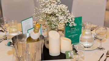 A table set for a formal event with a menu, a vase of flowers, candles, and a bottle of champagne.