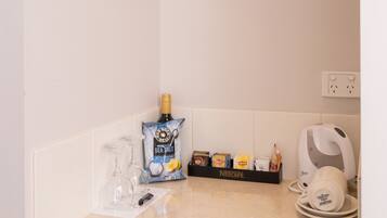A kitchen with a white countertop, a coffee maker, a Nescafé coffee machine, and a bottle of champagne.