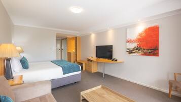 A modern hotel room with a bed, desk, TV, and artwork.