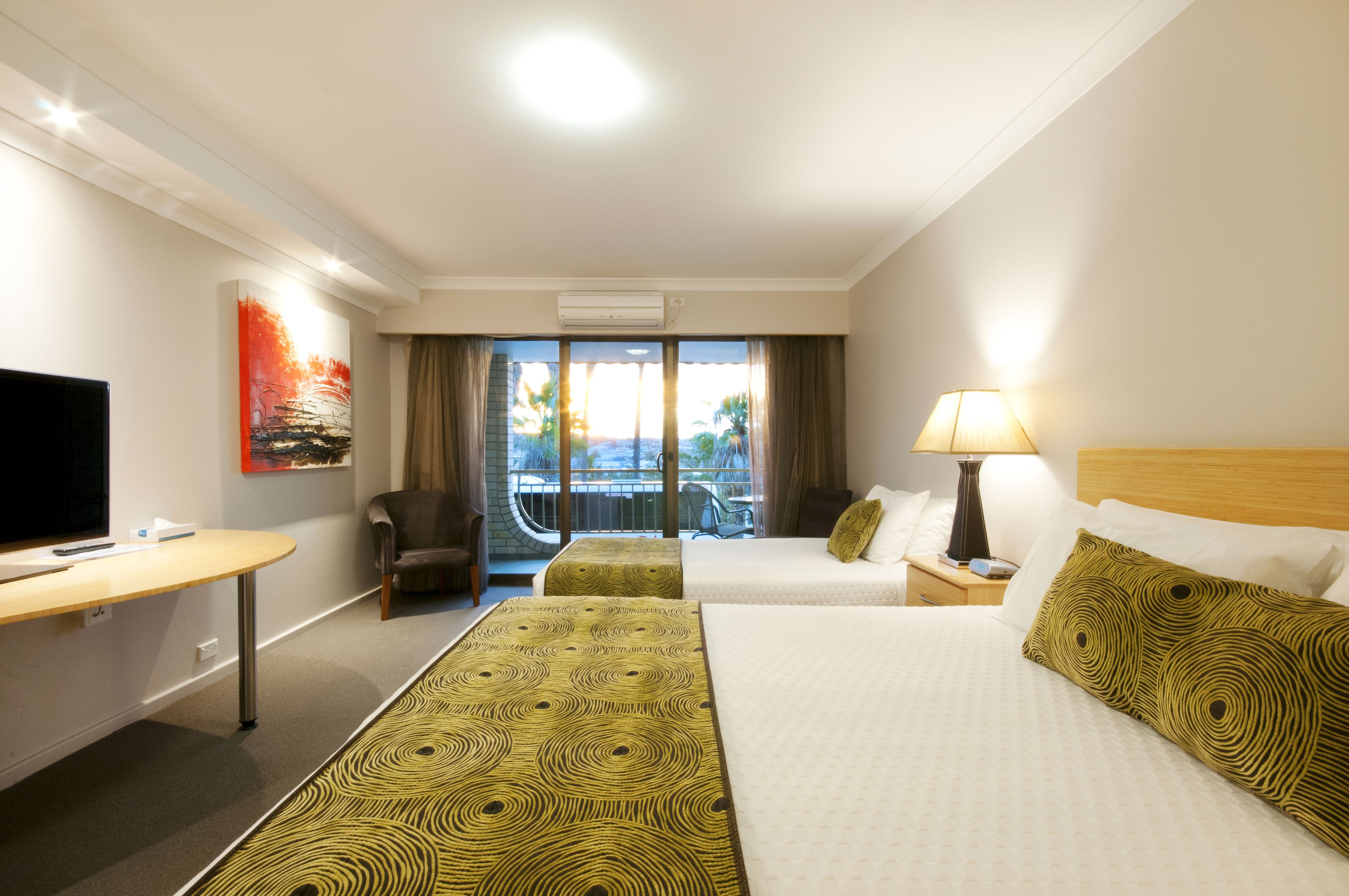 A hotel room with a TV, a desk, two beds, a chair, a balcony with a view, and a painting on the wall.