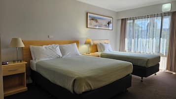 Une chambre d’hôtel avec deux lits, une table de chevet avec une lampe, un tableau au mur et une fenêtre avec des rideaux.