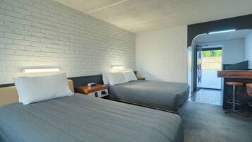 A room with two beds, a wooden nightstand, a desk with a chair, and a view of the outdoors.