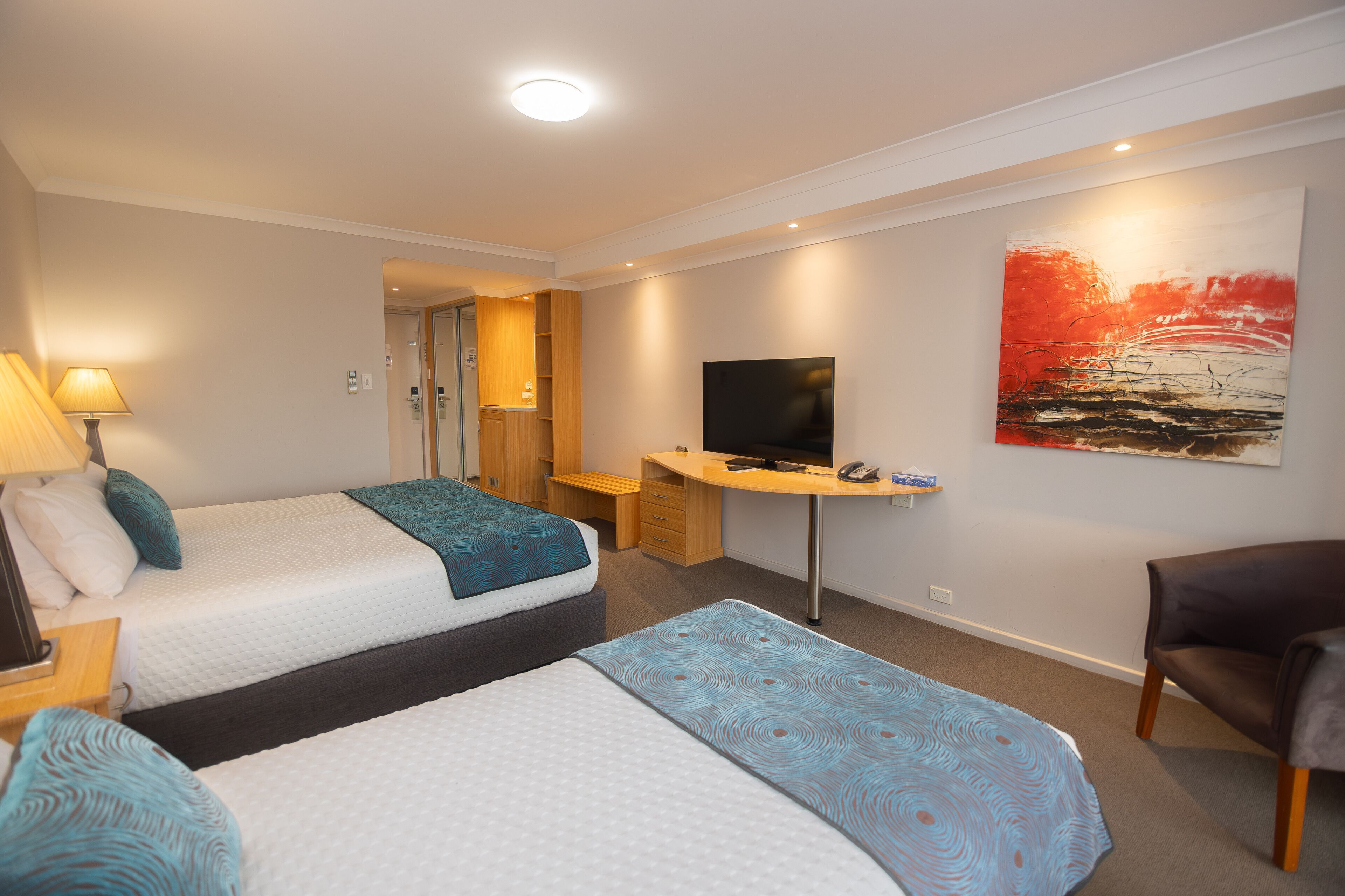 A hotel room with two beds, a desk, a TV, and a chair.