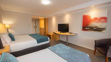 A hotel room with two beds, a desk, a TV, and a chair.