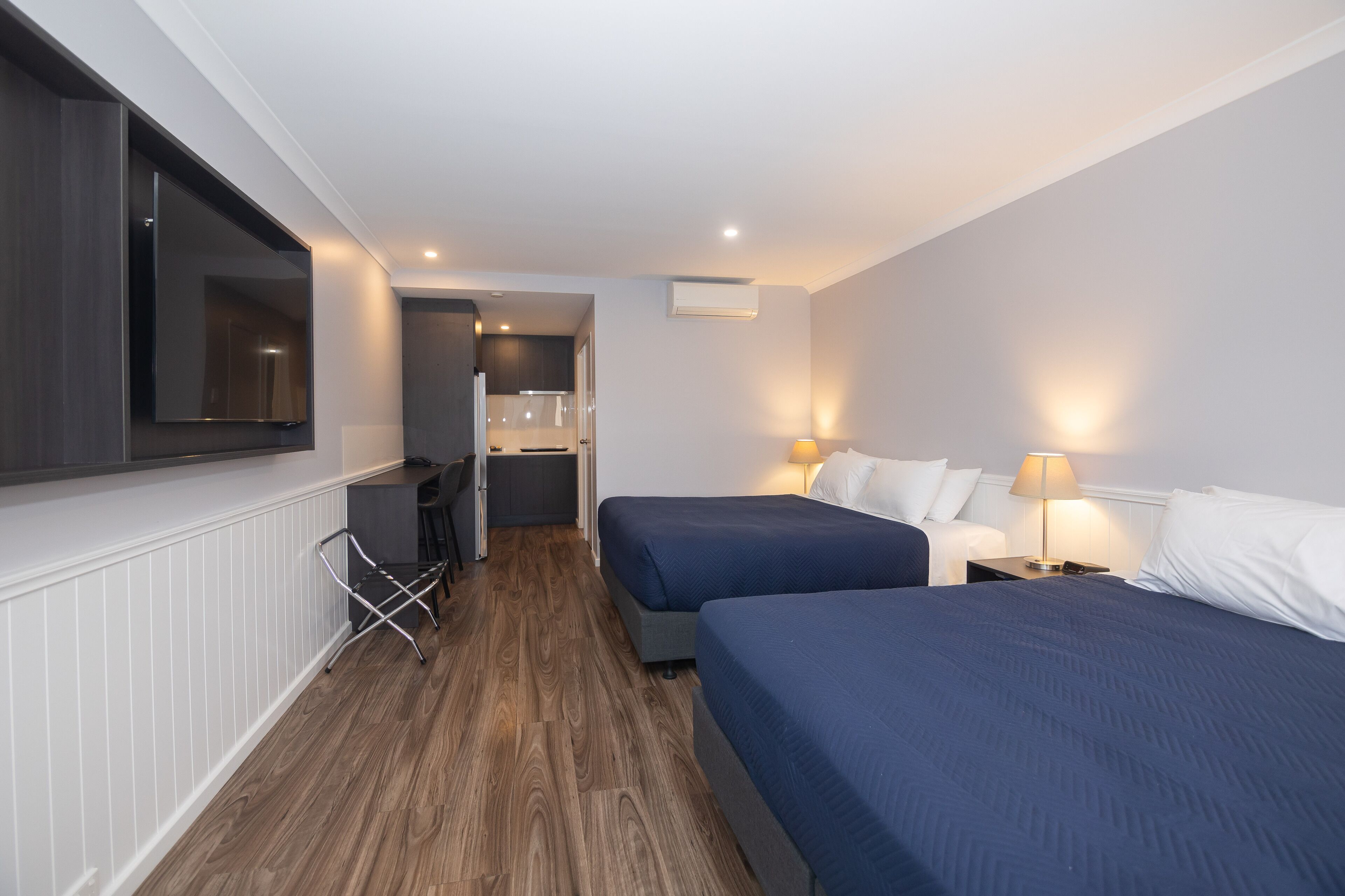 Habitación de hotel con dos camas, televisión, escritorio y kitchenette.