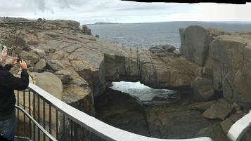 A person taking a photo of a rocky coastal landscape with a narrow passage between large boulders.