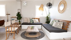 A modern living room with a sofa, chairs, a coffee table, and a fan. - Stoke Beach House - Hostel (Manly)
