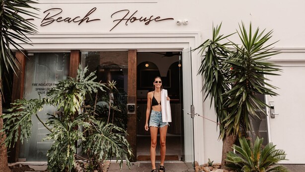 A woman standing at the entrance of a building labeled "Beach House." - Stoke Beach House - Hostel (Manly)