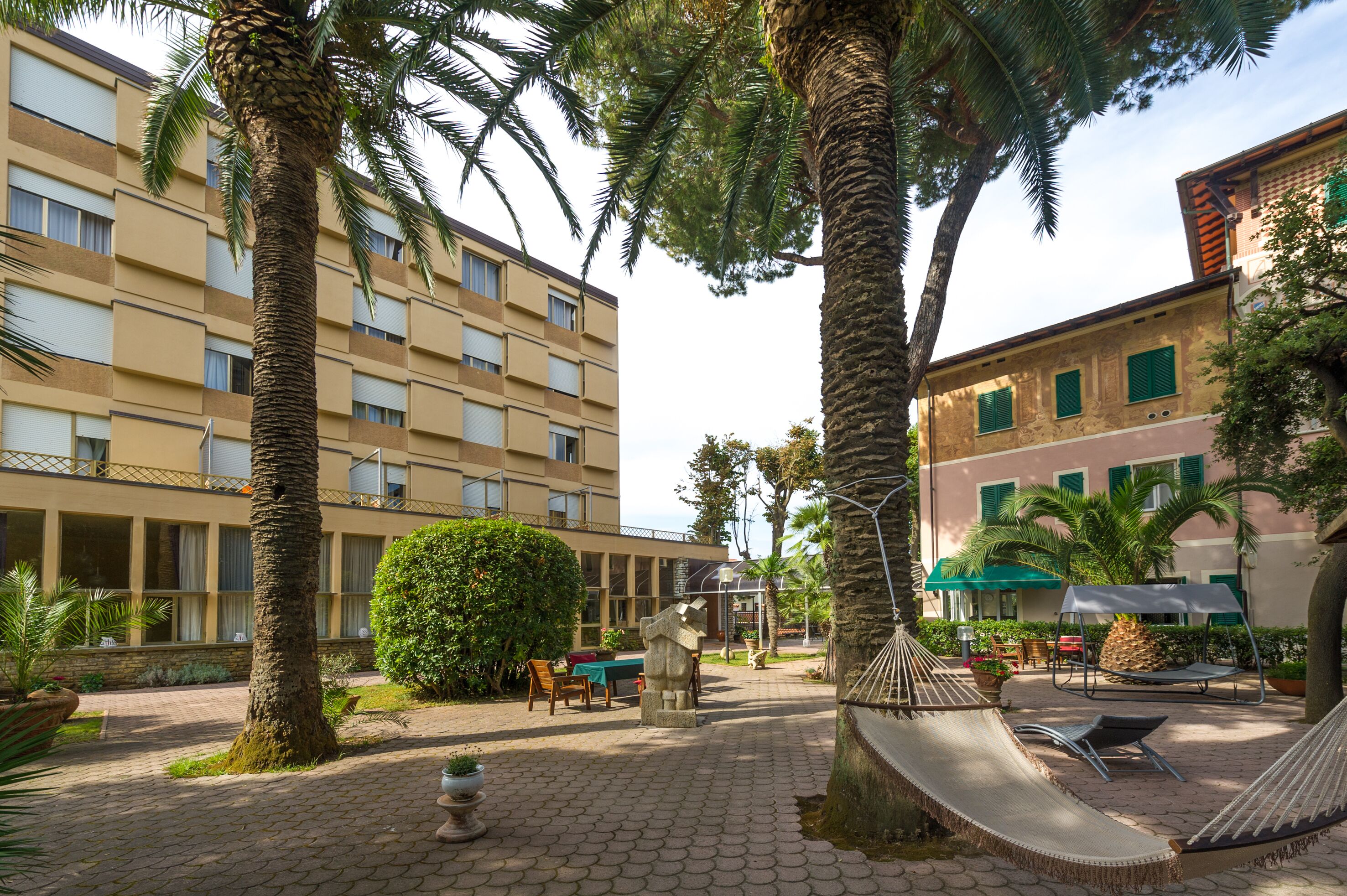A courtyard with palm trees, a hammock, and a table with chairs.